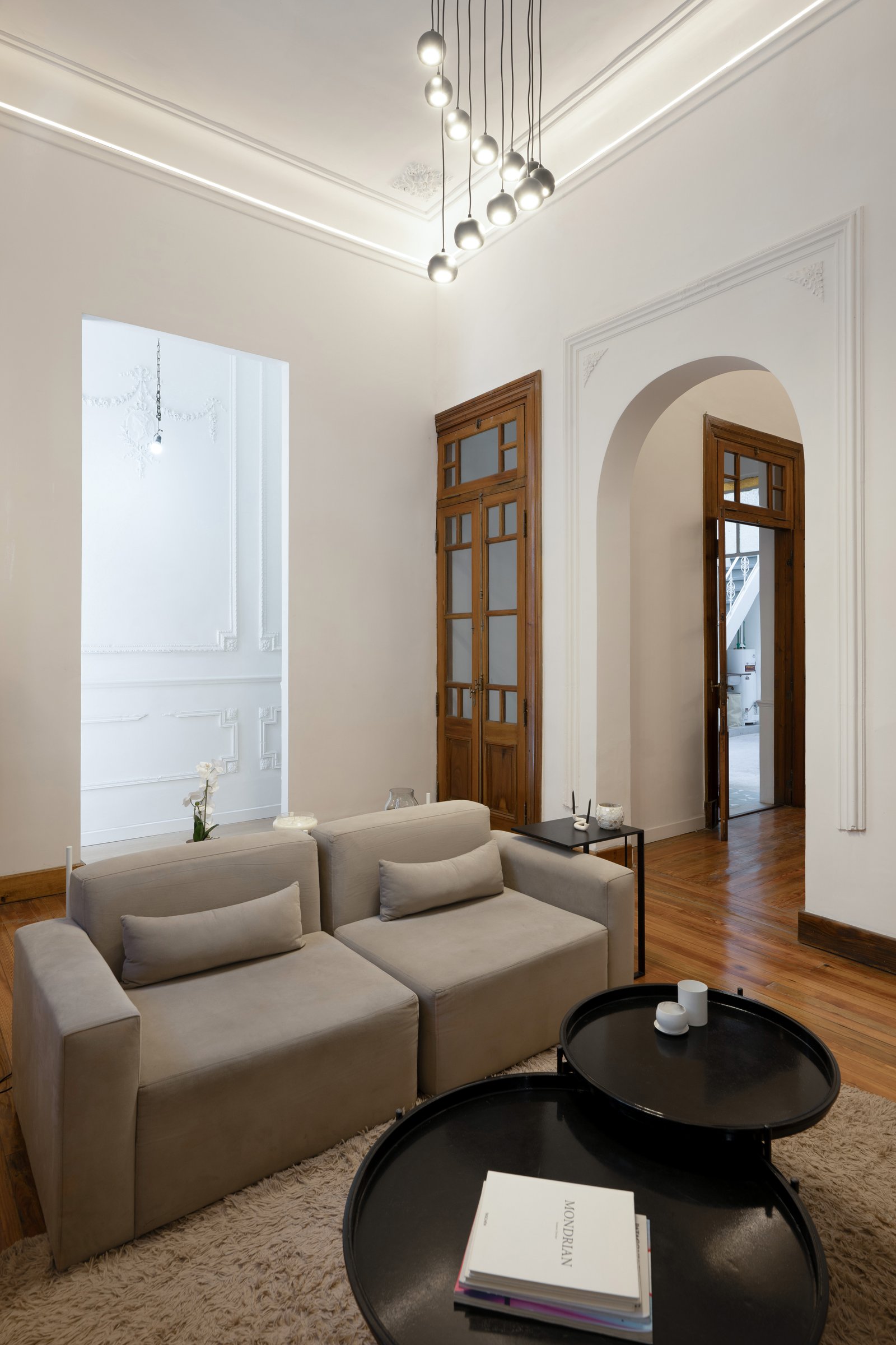 Living moderno con sofá modular, puertas de madera y luces colgantes — proyecto Casa Gainza, por Estudio Plats, en Caballito